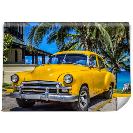 Żółty amerykański klasyczny samochód zaparkowany pod palmami na plaży w Varadero na Kubie 