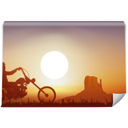 Motocyklista na tle zachodu słońca w pomarańczowym i niebieskim odcieniu