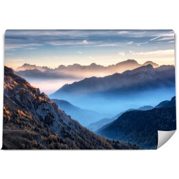Góry we mgle na piękny zachód słońca jesienią w Dolomitach, Włochy. Krajobraz z alpejską doliną górską, niskie chmury, drzewa na wzgórzach, wieś we mgle, niebieskie niebo z chmurami. Widok z powietrza. Passo Giau