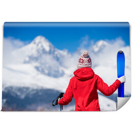Młoda kobieta z nartami spoglądająca na góry