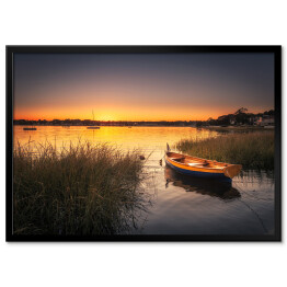 Plakat w ramie Mała łódka w trawie na jeziorze o zmierzchu