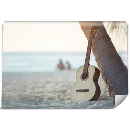 Gitara akustyczna stojąca na piaszczystej plaży pod palmą