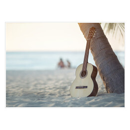 Gitara akustyczna stojąca na piaszczystej plaży pod palmą