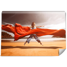 Kobieta unosząca się nad plażą w czerwonych tkaninach