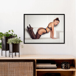 Plakat w ramie Kobieta w uwodzicielskiej czarnej bieliźnie siedząca na kanapie w pończochach