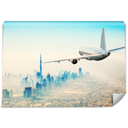 Fototapeta Samolot latający nad nowoczesnym miastem w jasnych barwach