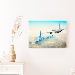 Obraz na płótnie Samolot latający nad nowoczesnym miastem w jasnych barwach