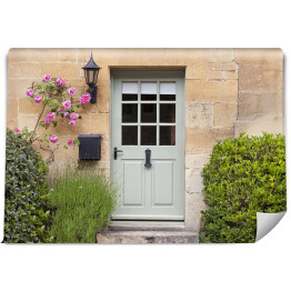 Jasne drewniane drzwi w starej tradycyjnej angielskiej chałupie w otoczeniu wspinaczki róż i lawendy