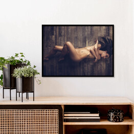 Plakat w ramie Młoda naga kobieta leżąca na drewnianej podłodze