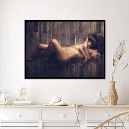 Plakat w ramie Młoda naga kobieta leżąca na drewnianej podłodze