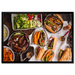Plakat w ramie Grill - kiełbasa, kanapki ze smażonymi ziemniakami i sosem podawanymi na rustykalnym stole