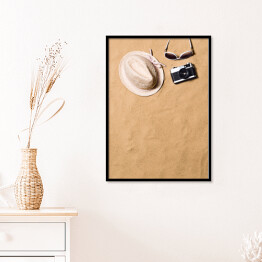 Plakat w ramie Okulary przeciwsłoneczne, wiklinowy kapelusz i aparat fotograficzny na piasku