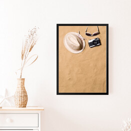 Obraz w ramie Okulary przeciwsłoneczne, wiklinowy kapelusz i aparat fotograficzny na piasku