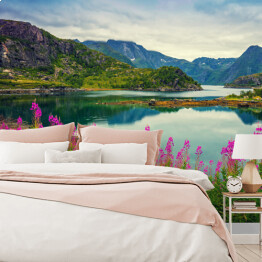 Fototapeta winylowa zmywalna Widok na norweski fiord, skaliste wybrzeże, pochmurne błękitne niebo i kwitnące różowe kwiaty