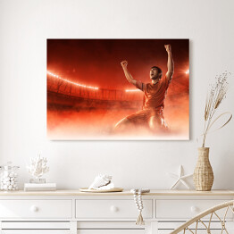 Obraz na płótnie Piłkarz świętuje bramkę na przydymionym czerwonym tle 