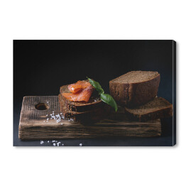 Obraz na płótnie Chleb żytni z wędzonym łososiem, sól morska i świeża bazylia na drewnianej desce 