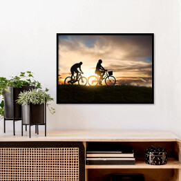 Plakat w ramie Młoda para jadąca rowerami o zachodzie słońca