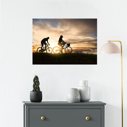 Plakat Młoda para jadąca rowerami o zachodzie słońca