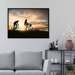 Plakat w ramie Młoda para jadąca rowerami o zachodzie słońca