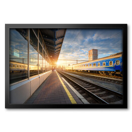 Obraz w ramie Niebieski pociąg pasażerski na stacji kolejowej o zmierzchu