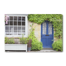 Obraz na płótnie Ciemnoniebieskie drzwi w starym tradycyjnym angielskim kamiennym domku otoczonym różową różą, bluszczem i żywopłotami