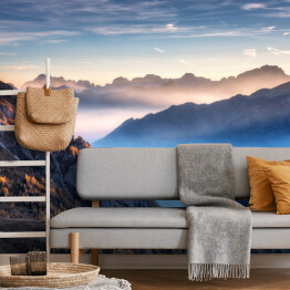 Fototapeta Góry we mgle na piękny zachód słońca jesienią w Dolomitach, Włochy. Krajobraz z alpejską doliną górską, niskie chmury, drzewa na wzgórzach, wieś we mgle, niebieskie niebo z chmurami. Widok z powietrza. Passo Giau