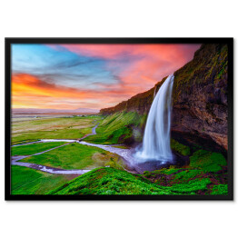 Plakat w ramie Piękny krajobraz z zielonymi równinami i wysokim wodospadem wylewającym się z pokrytej mchem kamiennej ściany