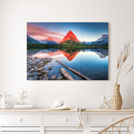 Obraz na płótnie Czerwona góra i jej lustrzane odbicie w jeziorze - widok z brzegu usłanego kamieniami